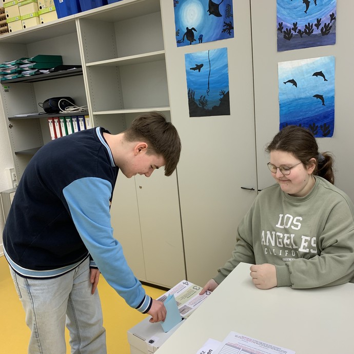 Schüler wirft seinen Wahlzettel in die Wahlurne (vergrößerte Bildansicht wird geöffnet)